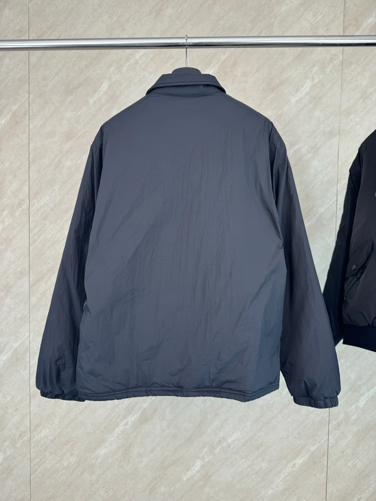 P670 25FW Ralph Lauren red label light cotton jacket (coach jacket) size s m l xl Fabric procurement: a combination of pragmatism and classic texture Material: high-density nylon taffeta Features: density is about 210T-300T, smooth and slightly matte surface, excellent windproof and waterproof performance (with DWR water-repellent treatment), strong wrinkle resistance and easy care, in line with the positioning of American casual "durable and practical".  Color: Classic dark black, using vat dyeing process (dye penetrates into the fiber), the color fastness reaches ISO level 4 or above to avoid fading or color transfer after washing.  2. Lining fabric Material: Lightweight cotton-polyester blended lining (65% Polyester + 35% Cotton) Function: Reduce friction between the fabric and inner clothing, improve wearing smoothness; blended material has both breathability and durability to avoid the stuffy feeling of pure nylon lining.  Version and cutting process Version: Classic Coach Jacket, loose version, slightly dropped shoulder line (shoulder width is 1-2cm wider than the standard version), length to the hips, and slightly tapered straight sleeves, taking into account both freedom of movement and casual style.  Embroidery technology: Polo horse logo on the left chest: flat satin stitch embroidery (satin embroidery), embroidery thread: 100% polyester high color fastness embroidery thread (the color number is consistent with the brand’s standard red color card), stitch density 12-15 stitches/cm, the outline of the horse logo is clear, and the details of the rider and horse are burr-free.  Embroidery positioning: precise positioning through the template (12cm from the neckline and 8cm from the placket) to ensure left and right symmetry and centering.  Topstitching technology: The seams of the body are made of double-needle flat seams (needle pitch 3cm/10 needles), the stitches are smooth and straight, the stitching color is dark black (the same color as the fabric), and the stitch width is 0.5cm, which enhances firmness while forming simple decorative lines.  1. Main body splicing, splicing of the front placket and body: The placket is made of double-layer folding + flat seam splicing, with a thickness of about 0.3cm to ensure that the buttons are not easily deformed when fixed; the edges of the placket are cut with a hot knife to avoid burrs.  Sleeve panels are spliced ​​to the body: the armholes are spliced ​​with round-head keyhole machine seams + flat seams. After splicing, the armholes have a natural curvature and no sense of tightness during movement; the height of the sleeves is about 8-10cm, which is in line with the loose characteristics of casual jackets.  Main button: black urea resin button, matte surface treatment, buttonholes are hand-made keyholes (6 strands of cotton thread, keyhole density 8 stitches/mm), the edges of the eyelets are smooth and without burrs.  Collar buttons: The first button on the collar is a hidden button (diameter 12mm), which prevents the collar from opening and improves the neatness of wearing.